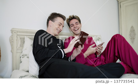Gay couple laughing together in bed with smartphone 137735541