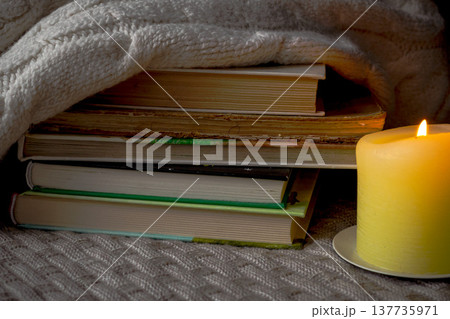 A stack of books and a warm sweater on a knitted plaid by candlelight 137735971