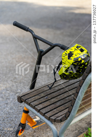 Helmet and children's sports scooter in the park near the bench 137736027