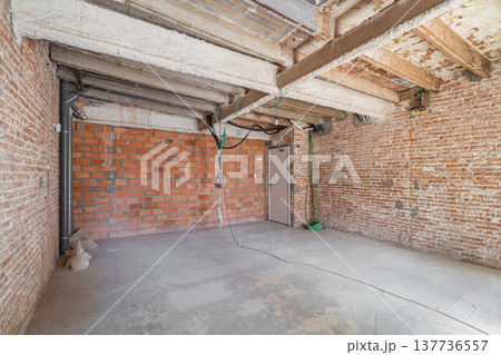 An empty room under renovation with exposed brick walls and concrete floor. The ceiling features wooden beams and electrical wiring is visible. 137736557