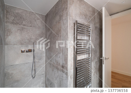 Modern bathroom with gray tiled walls, a shower with a handheld showerhead, and a heated towel rail. Bright and minimalistic design. Modern bathroom with gray tiled walls, a shower with a handheld showerhead, and a heated towel rail. Bright and minimalistic design. 137736558