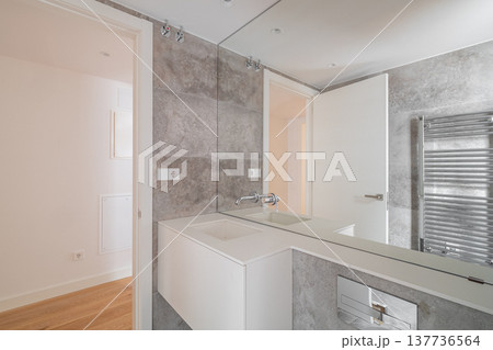 Modern bathroom with gray walls, a large mirror, and a sleek white sink. The space is well-lit and features a towel radiator. 137736564