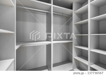 Empty modern closet with white shelves and hanging space. Minimalist design, organized storage area, suitable for home interiors. 137736567