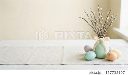 A serene Easter decoration featuring pastel-colored eggs arranged next to a mint green vase filled with pussy willow branches 137738107