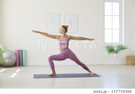 Sporty yogi fit woman doing yoga on mat in modern studio, Warrior II pose body strength and balance Sporty yogi fit woman doing yoga on mat in modern studio, Warrior II pose body strength and balance 137739366