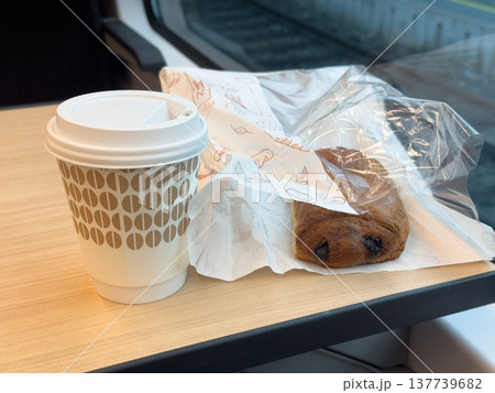 Sweet pastries in a paper bag and a glass of coffee to go on a table in a train 137739682