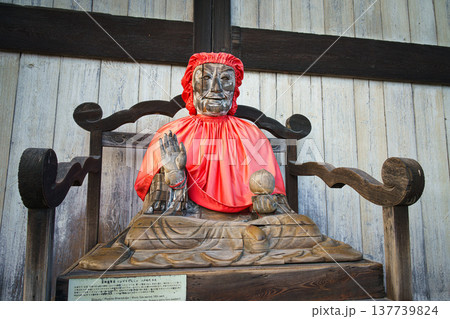 Nara, Japan - Sep 26 2024, close up view of Statue of Pindola Bharadvaja in front of Great Buddha Hall of Todaiji temple, sitting on a chair in red clothes, without people, Nara, Japan Nara, Japan - Sep 26 2024, close up view of Statue of Pindola Bharadvaja in front of Great Buddha Hall of Todaiji temple, sitting on a chair in red clothes, without people, Nara, Japan 137739824