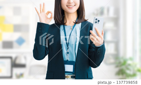 スマートフォンを持ってOKポーズをする笑顔の女性・ビジネスウーマン 137739858