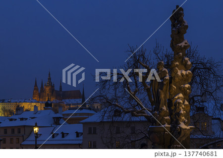 Prague Castle overseeing Charles Bridge with snowy Baroque statue at night 137740681