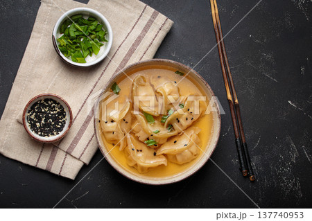 Gyoza dumplings broth soup chopsticks dark background bowl asian wontons 137740953