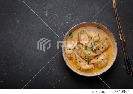 Gyoza dumplings broth soup chopsticks dark background bowl asian wontons 137740964