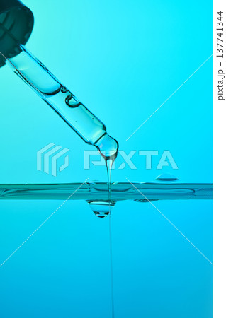 Dropping serum liquid from pipette into blue water 137741344