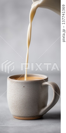 Milk pouring from pitcher into ceramic mug. Creamy dairy milk pouring from a pitcher into a ceramic mug on a gray table 137741369