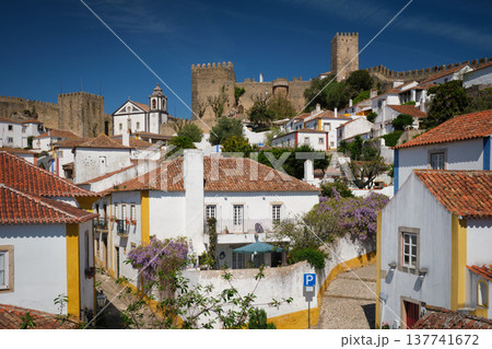Obidos town featuring white houses, vibrant rooftops, and the impressive medieval castle under a blue sky. Portugal Obidos town featuring white houses, vibrant rooftops, and the impressive medieval castle under a blue sky. Portugal 137741672