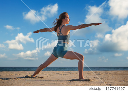 A woman practices Warrior 2 Virabhadrasana 2 pose on the beach during sunset, embodying strength and peace in her yoga practice. A woman practices Warrior 2 Virabhadrasana 2 pose on the beach during sunset, embodying strength and peace in her yoga practice. 137741697