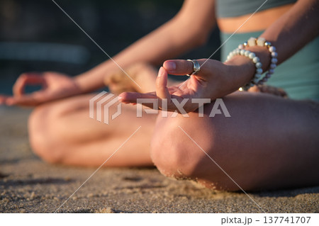 Woman meditates in Padmasana on the beach, using Chin mudra hand gesture in a tranquil setting during sunset. Woman meditates in Padmasana on the beach, using Chin mudra hand gesture in a tranquil setting during sunset. 137741707