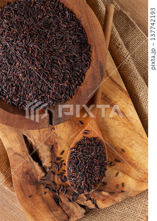 Natural black rice in a wooden bowl and spoon on a wooden surface in rustic style, top view Natural black rice in a wooden bowl and spoon on a wooden surface in rustic style, top view 137742193