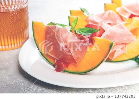 Cantaloupe melon with prosciutto and fresh basil, on a white plate, natural light, Cantaloupe melon with prosciutto and fresh basil, on a white plate, natural light, 137742203