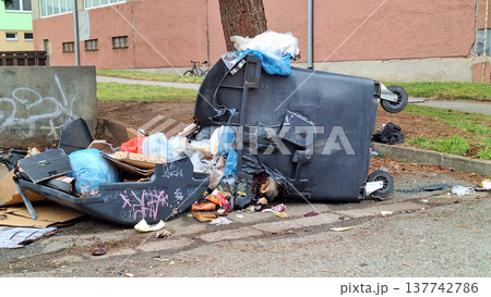 Overturned garbage bin spilling trash onto the street, creating an unsightly mess Overturned garbage bin spilling trash onto the street, creating an unsightly mess 137742786