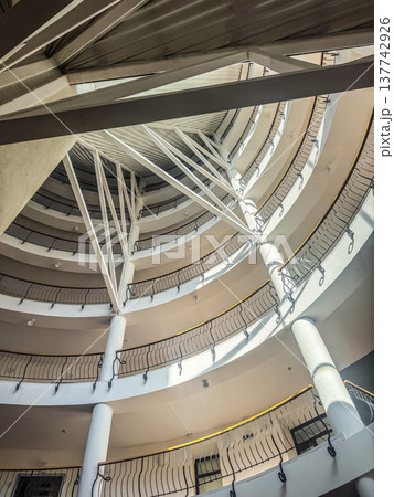 Looking up at the modern architectural design of a multi-story circular atrium with spiral balconies and a complex roof structure. Looking up at the modern architectural design of a multi-story circular atrium with spiral balconies and a complex roof structure. 137742926