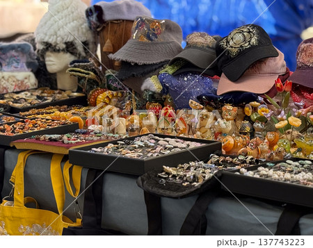 Handmade accessories and hats fill a colorful market stall with figurines and jewelry. Craft culture, gift shopping, creative abundance, and the playful charm of small artisan trade. 137743223
