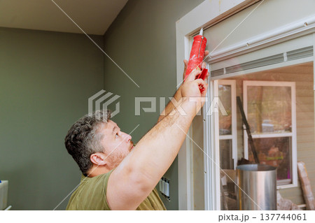 Man applies caulk to window frame in home in while preparing for repairs Man applies caulk to window frame in home in while preparing for repairs 137744061