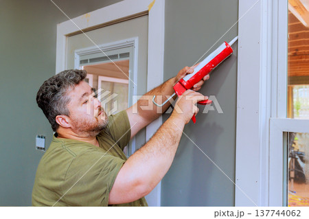 Man applies caulk to wall frame in home improvement project Man applies caulk to wall frame in home improvement project 137744062