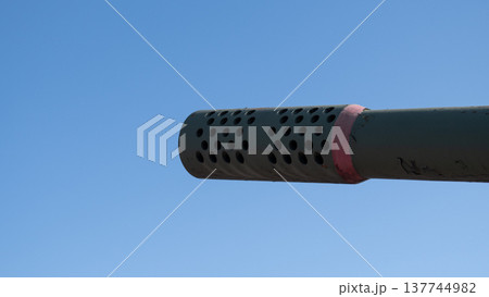 Perforated Muzzle Brake Closeup Under Blue Sky, Circular Hole Pattern And Vented Shroud For Recoil Control Visible, Clean Composition Emphasizing Functional Geometry And Industrial Texture 137744982