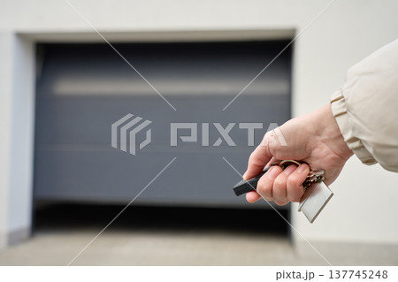 Closeup of hand holding garage remote and keys in front of closed garage door 137745248
