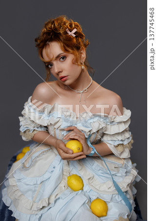 Young woman in Rococo dress holding lemon and blue ribbon against grey background Young woman in Rococo dress holding lemon and blue ribbon against grey background 137745468