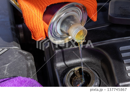Mechanic carefully pours golden oil into the engine while sunlight shines on the vibrant tools and equipment scattered nearby Mechanic carefully pours golden oil into the engine while sunlight shines on the vibrant tools and equipment scattered nearby 137745867