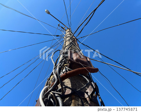 Beneath a vast blue sky, a sturdy concrete pole stands tall with numerous wires sprawling outwards, connecting homes and powering the community 137745871