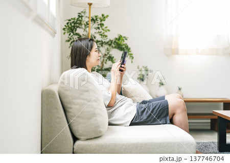 家のソファーでスマホをいじる若い女性 家のソファーでスマホをいじる若い女性 137746704