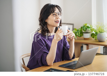 家のリビングでノートパソコンを開いてコーヒーを飲む50代のミドル女性 137746728