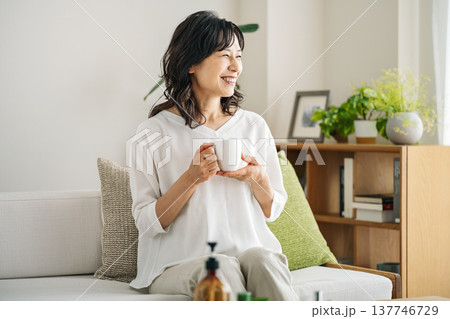 自宅のソファーでのんびりコーヒーを飲む50代のミドル女性 自宅のソファーでのんびりコーヒーを飲む50代のミドル女性 137746729