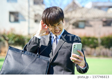 スマホを見て頭を抱え、苦悩する若いビジネスマン 上半身 137746813