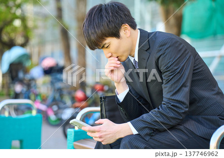 園のベンチでスマホを見て落ち込む若いビジネスマン 上半身 園のベンチでスマホを見て落ち込む若いビジネスマン 上半身 137746962
