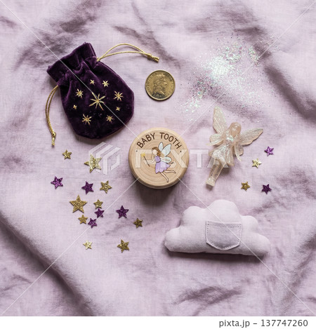 A whimsical flat lay arrangement for the tooth fairy featuring a baby tooth box, purple pouch, gold coin, sparkles, and a little fairy toy.High quality photo 137747260