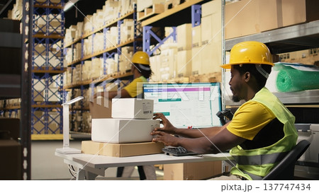 African american man using scanner to process barcode and stick shipping labels on boxes from industrial storage racks. Scanning awb on adhesive tags for package tracking service. Camera A. African american man using scanner to process barcode and stick shipping labels on boxes from industrial storage racks. Scanning awb on adhesive tags for package tracking service. Camera A. 137747434