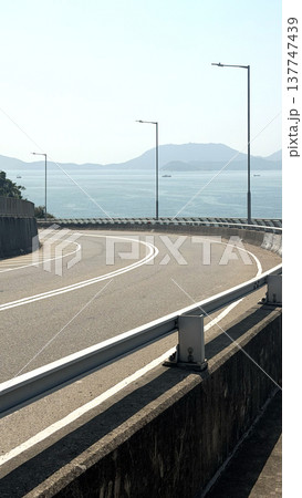 Curving highway overpass with ocean and distant mountains under a clear sky Curving highway overpass with ocean and distant mountains under a clear sky 137747439