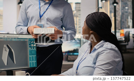 Employees talking, evaluating advanced solar cell technology alternative energy device. R and D office coworkers test solar panel lamp prototype, checking maximum power levels, camera B 137747522
