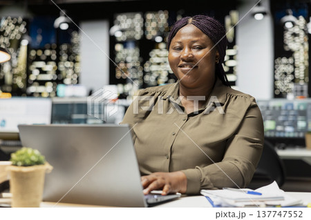 Portrait of smiling analyst working after hours on finances at the office, fact checking numbers and data metrics. Organizing the agenda for upcoming administrative tasks, management. 137747552