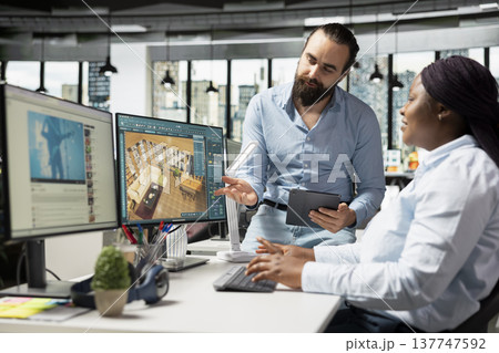 Team of diverse architectural specialists working with CAD program on computer, modern apartment layout with floor plan. 3D rendering software on dual monitors, interior design. 137747592