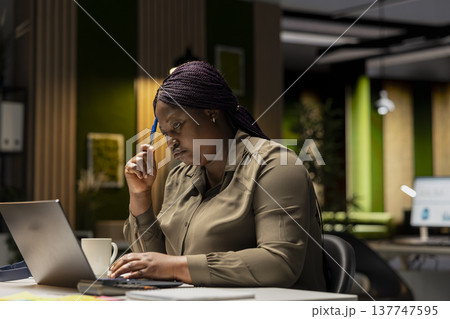 African american associates reflecting on a problem late at night in the office, methodical planning and critical thinking to guide her toward a decision that balances rationality with innovation. 137747595