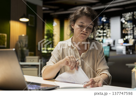 Businesswoman makes mistake in transcribing finance updates on notebook, tearing up the paper sheet and restarting. Discontent impatient worker wanting to finish tasks for the night. 137747598