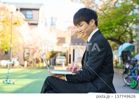 公園のベンチに座り真剣な表情でスマホを見る新人ビジネスマン 上半身 137749626