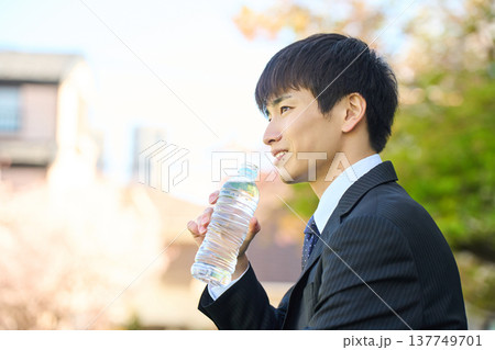 公園でペットボトルの水を飲みリフレッシュする新人ビジネスマン 上半身 横顔 公園でペットボトルの水を飲みリフレッシュする新人ビジネスマン 上半身 横顔 137749701