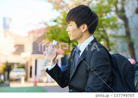 外回り中に公園で水分補給をして笑顔を見せる新人ビジネスマン 上半身 外回り中に公園で水分補給をして笑顔を見せる新人ビジネスマン 上半身 137749705