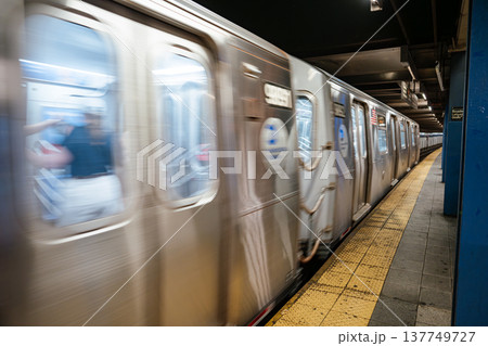 Blurred New York City subway train moving along the platform at Broadway Lafayette Street station. Underground urban transit system showing speed, stainless steel cars, and yellow safety strip. 137749727