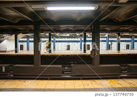 A commuter walks across the Broadway Lafayette Street subway platform in New York City. Underground metro station with tiled walls, steel beams, and urban public transportation setting. A commuter walks across the Broadway Lafayette Street subway platform in New York City. Underground metro station with tiled walls, steel beams, and urban public transportation setting. 137749730